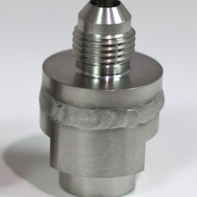 A metal fitting with a threaded top and visible weld seam around the middle, standing on a white surface.