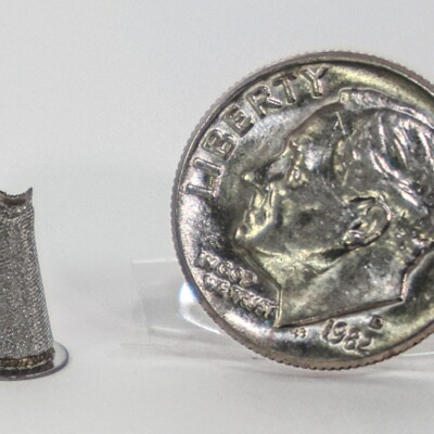A small metal cone is displayed next to a 2015 U.S. dime for size comparison on a white background.