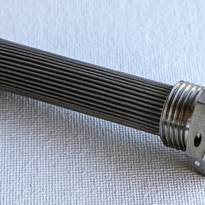A cylindrical metal filter element with threaded ends is placed on a light textured surface.
